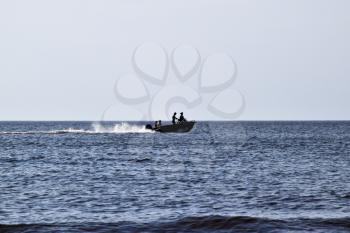 The boat rushes by the sea. In the boat people. Seascape in the evening. Silhouette of a motor boat and people in it against the background of the sea distance.