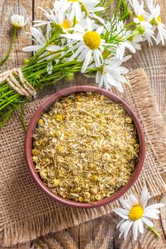 Dried and fresh chamomile flowers and leaves on wooden rustic background, alternative medicine