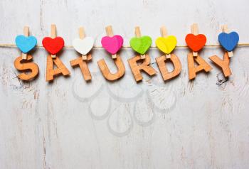 Saturday word from wooden letters with colored clothespins on a white wooden background