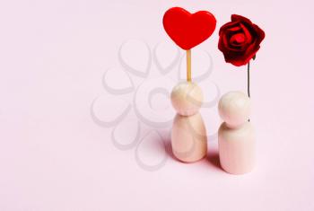 Female wooden figure with heart and male with flower on  pink background. Concept of love, romance