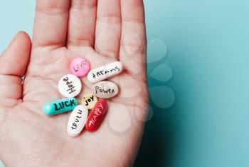 The concept of creative pills, a placebo in the hand, with joy, love, happiness, truth, power, dream on a blue background