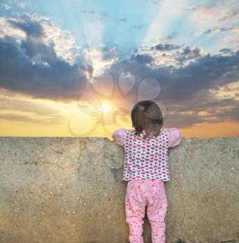 Little girl looking for a wall to the sunset sky . Conceptual design.