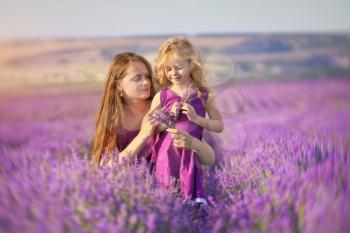 Little girl and mother at meadow of lavender. Family care and nature composition.