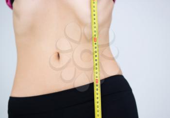 Sport, fitness and diet concept - close up of trained belly with measuring tape