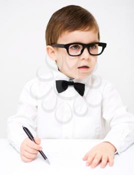 Little boy is drawing on white paper using pen