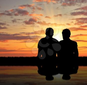 Concept of gay people. Silhouette of two gay holidaymakers near the river at sunset
