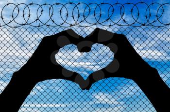 Concept of the refugees. Silhouette of the heart out of the hands on the background of the fence near the border
