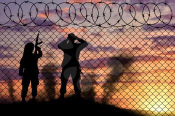 Concept of terrorism. Silhouette scouts terrorists near the border fence at sunset in smoke