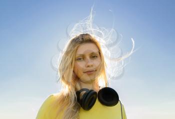 Concept of music. Young woman with headphones on the sky background