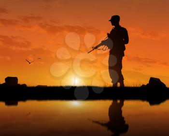 Silhouette of a terrorist with a weapon at sunset near the river. The concept of terrorism and war