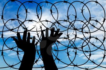 concept of the refugees. Silhouette of a hand outstretched to the sun in the sky background barbed wire