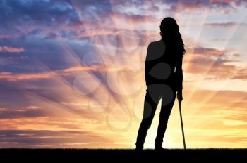 Silhouette of a disabled woman supports herself with a crutch admiring the sunset. The concept of people disabled with crutch