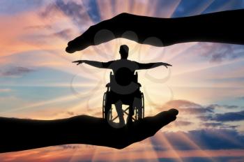 Silhouette of happy disabled man in wheelchair in hands of help. The concept of protection and help to people with disabilities