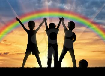 Childhood concept. Three happy children holding hands on a background of a rainbow at sunset
