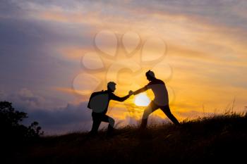 Teamwork couple hiking help each other trust assistance silhouette in mountains, sunset. Teamwork of two men hiker helping each other on top of mountain climbing team, beautiful sunset landscape.