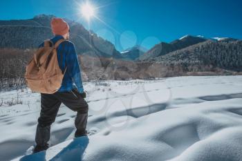 Man with backpack trekking in mountains. Cold weather, snow on hills. Winter hiking. Sun and snow