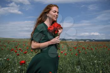 Beautiful young red-haired girl with freckles on a beautiful poppy field.