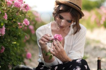 Beautiful young woman with curly hair posing near roses in a garden. The concept of perfume advertising.