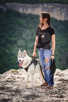 Beautiful girl plays with a dog, grey and white husky, in the mountains at sunset. Indian girl and her wolf