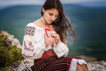 Attractive woman in traditional romanian costume on mountain green blurred background. Outdoor photo. Traditions and cultural diversity