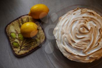 Lemon meringue pie on cutting board on brown wooden background. Preparation of lemon tart.