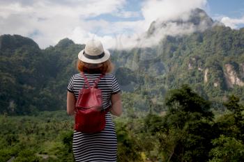 Redhair woman traveler with backpack and hat and looking at amazing mountains and forest, travel holiday relaxation concept.
