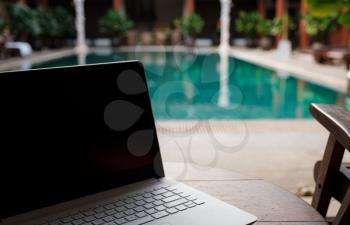 A white laptop on wooden table swiming pool background. A start of new day. Freelance business concept. Flexible remote working, travelling, advert and copy space