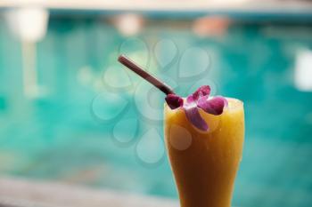 fresh tropical smoothie or mango juice in a tall glass on the background of the pool