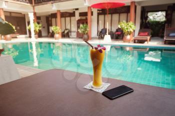 Smartphone and mango smoothie in a tall glass on a sunbed near the swimming pool. Idea and concept of vacation, travel and discoveries