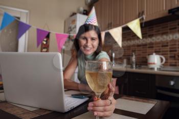 Girl celebrating birthday online in quarantine time. Woman celebrating her birthday through video call virtual party with friends. Authentic decorated home workplace. Coronavirus outbreak 2020.