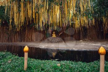 Golden buddhist pagoda statue near tree with traditional yellow flags in outdoor temple in Chiang Mai in Northern Thailand