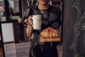 Close up female hand serving hot latte art coffee in white cup and croissant on wooden plate in coffee shop. Cafe drinking menu hot coffee at restaurant. Breakfast menu in the morning time.