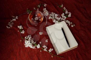 Spring flat lay top view home office workspace - notebook with tea cup and cherry blossom branches on a red desk background