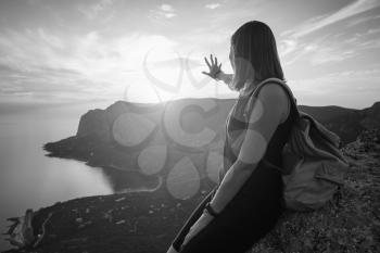 Young woman with a backpack enjoys the view of the mountains and the sea at sunset. Lifestyle emotional concept vacations weekend getaway aerial Crimea landscape