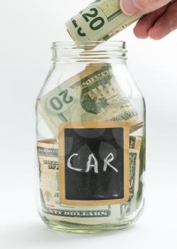 Caucasian hand putting money into glass jar on white background with black chalk label or panel and used for saving US dollar bills for car expenses