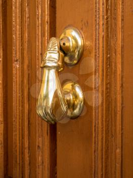 Side view of brass door knocker shaped like a hand on old wooden door