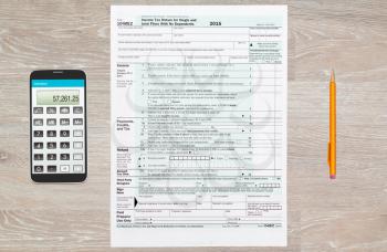Washington DC, USA - February 12, 2016: USA IRS tax form 1040EZ for year 2015 with pencils and calculator app on smartphone on wooden desk and taken from above