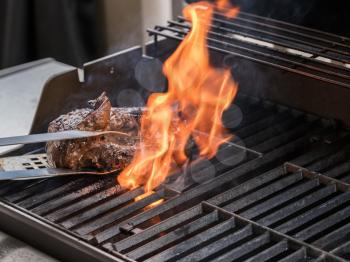 Close up of large piece of steak or beef flaming on barbeque