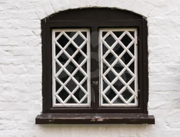Diamond shaped glass in wooden frame in old stone cottage painted in white.