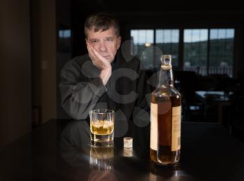 Senior adult male facing a kitchen table with alcoholic drink and looking very sad and depressed