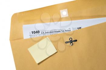 Printed Form 1040 for income tax return in brown envelope with blank yellow sticky note for copy