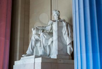 Red and blue pillars illuminate the white statue of President Lincoln in Lincoln Memorial in Washington DC in illustration of US flag