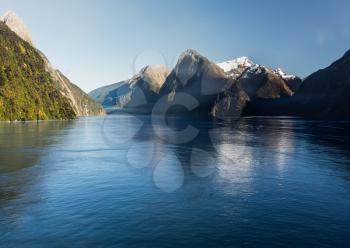 Sailing into Milford Sound on South Island of New Zealand in early morning as the sun rises above the mountains