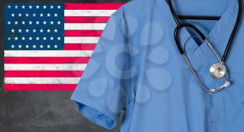 Blue doctor scrubs shirt and stethoscope hang empty in front of USA flag. Illustration of healthcare system needing immigrants to help with staffing issues