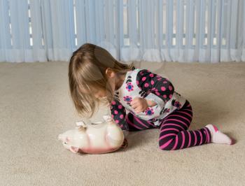 Young girl on floor of home trying to get money to pay off debt  out of a piggy bank for expenses in the future