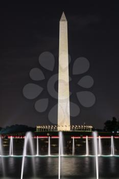 Washington Monument stands over World War 2 memorial and fountains at night in Washington DC