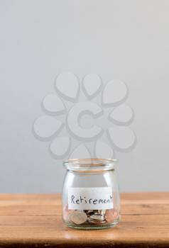 Loose change and coins inside a glass jar against a grey background to represent lack of retirement savings