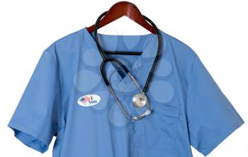Blue medical scrubs uniform shirt hanging on a hanger with stethoscope with I Vote sticker to illustrate healthcare issues