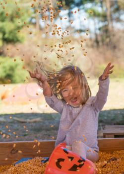 Young caucasian girl playing in the seeds from corn kernels and throwing them into the air at halloween pumpkin patch
