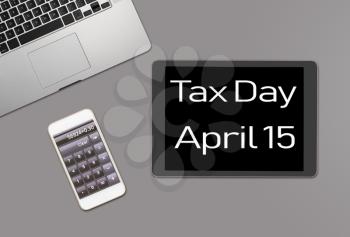 Overhead clean grey desk for laptop, smartphone and tablet computer with message for tax day 2019 as April 15